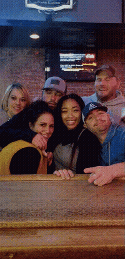 A Group Of People Posing For A Picture In Front Of A Sign That Says Dark Lager On It GIF