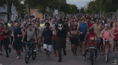 A Group Of People Running And Riding Bicycles With One Wearing A Red Shirt That Says Nike GIF