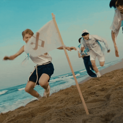 A Group Of People Running On A Beach With A Flag That Has The Letter P On It GIF