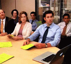 A Group Of People Sit Around A Table With A Laptop GIF