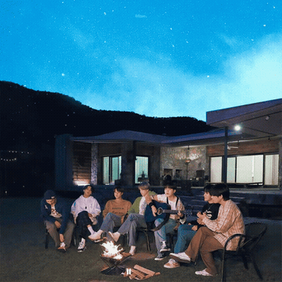 A Group Of People Sitting Around A Fire With One Wearing A Sweatshirt That Says ' Abercrombie ' On It GIF