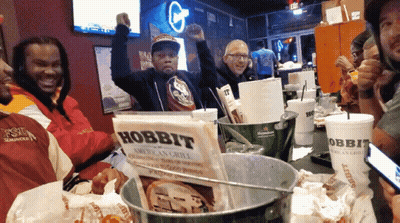 A Group Of People Sitting Around A Table With A Sign That Says Hobbit On It GIF