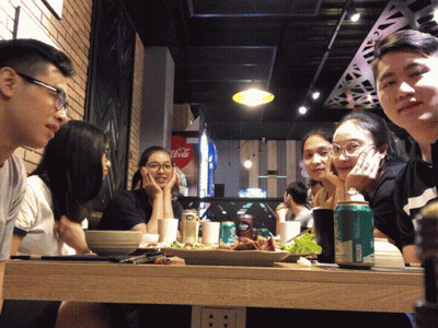 A Group Of People Sitting At A Table In Front Of A Coca Cola Fridge GIF
