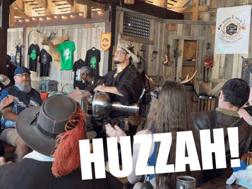 A Group Of People Sitting At A Table With The Word Huzzah On The Bottom Right GIF