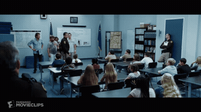 A Group Of People Sitting At Desks In A Classroom With A Sign That Says Movieclips GIF