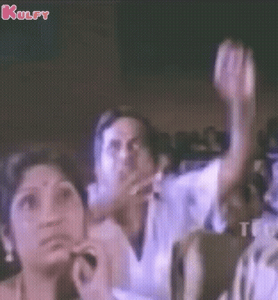 A Group Of People Sitting In A Dark Room With Their Hands In The Air GIF