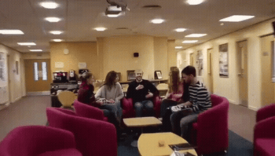 A Group Of People Sitting In Chairs In A Hallway GIF