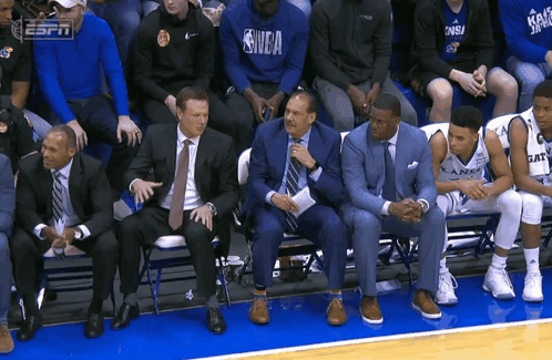 A Group Of People Sitting On A Bench With One Wearing A Shirt That Says Nba GIF