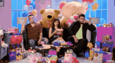 A Group Of People Sitting On A Couch With A Teddy Bear And Balloons In The Background GIF