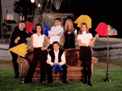 A Group Of People Standing Around A Couch With Umbrellas GIF