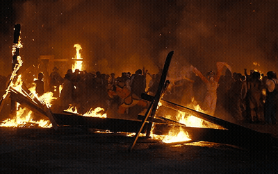 A Group Of People Standing Around A Large Fire GIF