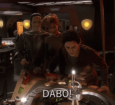 A Group Of People Standing Around A Roulette Table With The Word Dabo On It GIF
