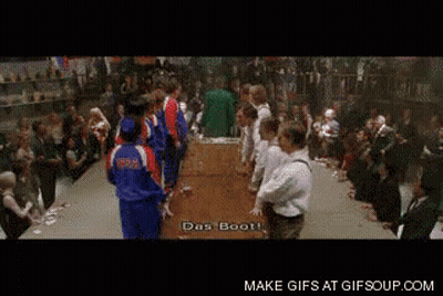 A Group Of People Standing Around A Table With The Words Das Boot Written On The Screen GIF