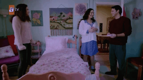 A Group Of People Standing In Front Of A Bed With A Tv Logo On The Wall GIF