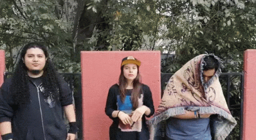 A Group Of People Standing In Front Of A Red Wall Including A Man With A Blanket On His Head GIF