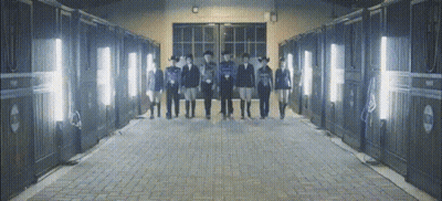 A Group Of People Standing In Front Of A Row Of Stable Doors GIF