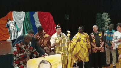 A Group Of People Standing In Front Of A Stage With A Man In A Yellow Robe Holding A Painting GIF