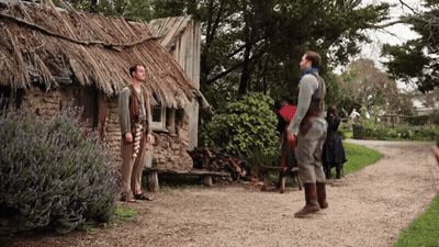 A Group Of People Standing In Front Of A Thatched Roof Building GIF
