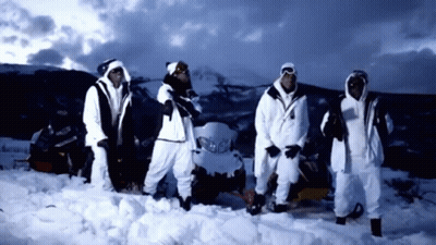 A Group Of People Standing In The Snow In Front Of A Snowmobile GIF