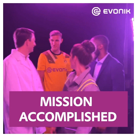 A Group Of People Standing Next To Each Other With A Purple Sign That Says Mission Accomplished GIF