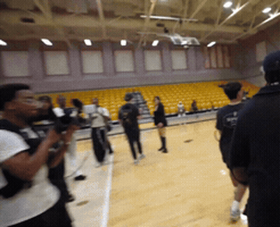 A Group Of People Standing On A Basketball Court With A Man Wearing A Black Shirt That Says ' Basketball ' On It GIF