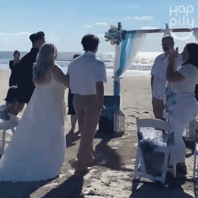 A Group Of People Standing On A Beach With A Sign That Says " Hap Oily " GIF