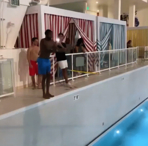 A Group Of People Standing On The Edge Of A Swimming Pool With The Number 70 On The Side GIF