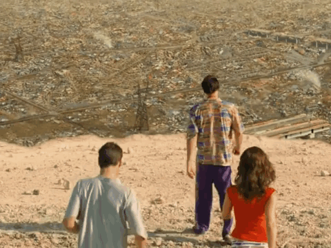 A Group Of People Standing On Top Of A Hill Looking Out Over A City GIF