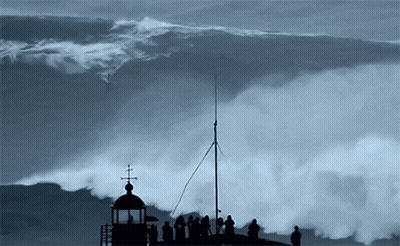 A Group Of People Standing On Top Of A Tower Watching A Large Wave GIF