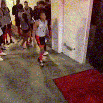 A Group Of People Walking Down A Hallway With A Red Rug GIF