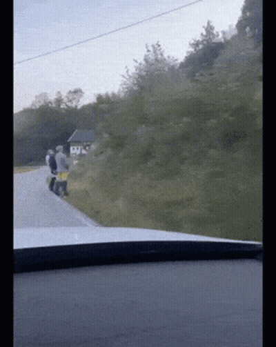 A Group Of People Walking Down A Road With A Small House In The Background GIF