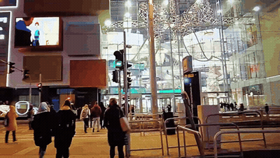 A Group Of People Walking Down A Street In Front Of A Building With A Sign That Says ' A ' On It GIF