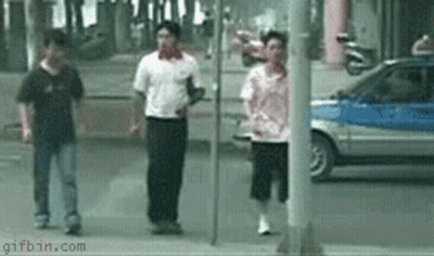 A Group Of People Walking Down A Street With A Car In The Background And A Gifbin.com Logo In The Corner GIF