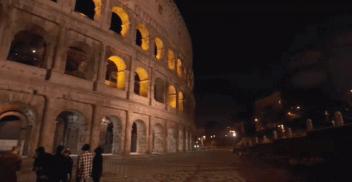 A Group Of People Walking In Front Of A Building That Has Arches On It GIF