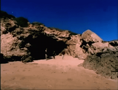 A Group Of People Walking Through A Cave On A Beach GIF