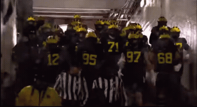 A Group Of People Wearing Black Uniforms With Yellow Numbers On Them GIF