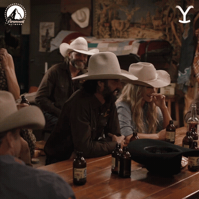 a group of people wearing cowboy hats sit at a table with bottles of beer and a paramount logo in the background