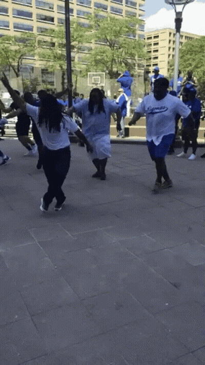 A Group Of People Wearing Dodgers Shirts Are Dancing On The Sidewalk GIF