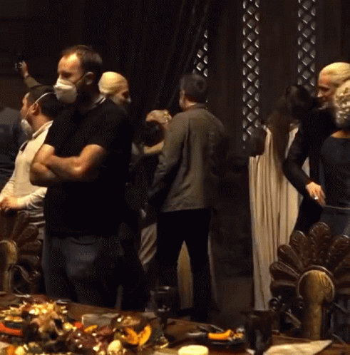 A Group Of People Wearing Face Masks Are Standing Around A Table Full Of Food GIF
