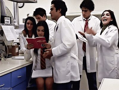 A Group Of People Wearing Lab Coats And Ties Are Standing Around A Table And One Of Them Is Holding A Book GIF