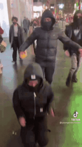 A Group Of People Wearing Masks And Hoodies Are Dancing In A Crowded Street . GIF