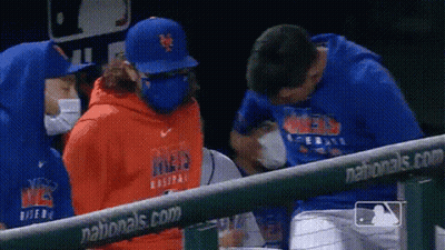A Group Of People Wearing Masks And Hoodies Are Standing Next To A Fence At A Baseball Game . GIF