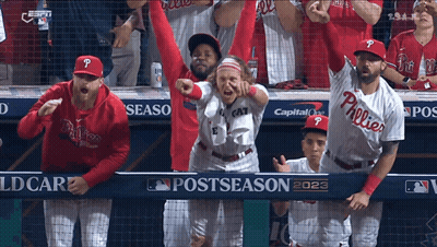 A Group Of Phillies Baseball Players Are Standing In The Dugout With Their Arms In The Air GIF