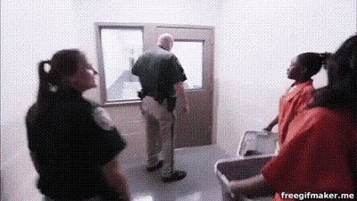 A Group Of Police Officers And Prisoners Are Standing In A Hallway Talking To Each Other . GIF