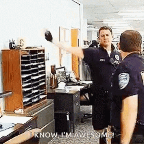 A Group Of Police Officers Are Standing In An Office Talking To Each Other And One Of Them Is Waving . GIF