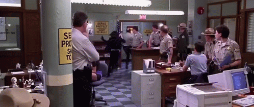 A Group Of Police Officers In A Police Station With A Sign That Says Serve Protect And Serve To Kill GIF