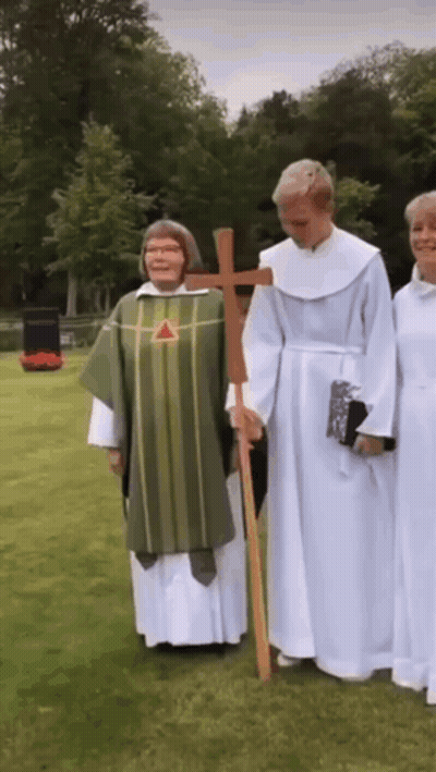 A Group Of Priests Are Standing In A Grassy Field Holding A Cross GIF