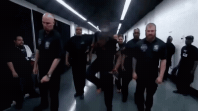 A Group Of Security Guards Are Walking Down A Hallway In A Building . GIF