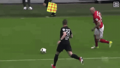 A Group Of Soccer Players Are Playing On A Field With A Referee Holding A Yellow Flag In The Background GIF