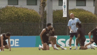 A Group Of Soccer Players Are Stretching On A Field In Front Of A Sign That Says ' Ade ' GIF